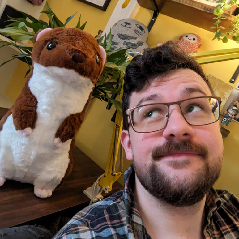 A photo of Brian Tyrrell. He has short black hair, an upper lip moustache, and stubble. He is holding a white labrador in his arms.